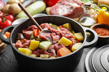 Cooking stew. Uncooked meat, vegetables and pot on black table