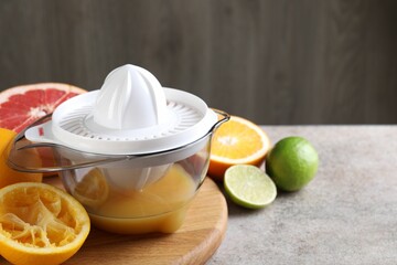 Plastic juicer and different citrus fruits on grey table, closeup. Space for text