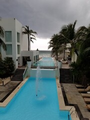 Long narrow pool looking out on the ocean, palm trees and chairs line to pool at this tropical resort.