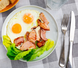 Fried eggs with slices of chicken and lettuce on a white plate. Delicious protein lunch