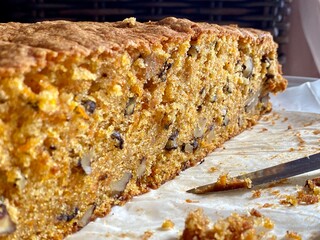Carrot sponge cake, cut in half, shows off the texture: grated carrots, walnuts, moist crumb. Sponge crumbs and a knife nearby
