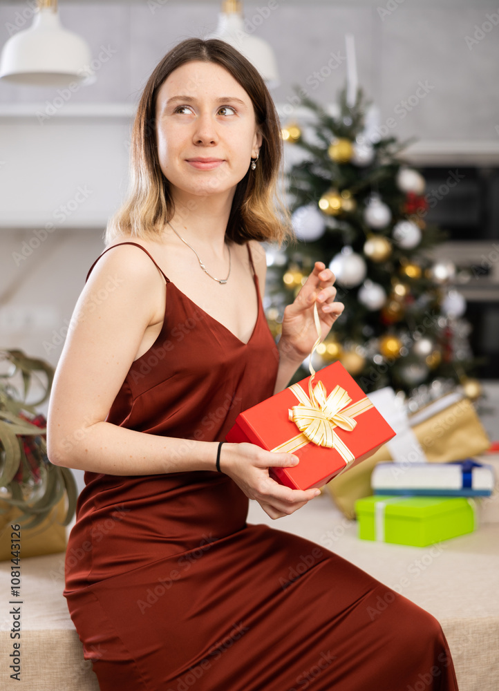 Wall mural Concentrated young woman wants to open a Christmas present while at home. Close-up image