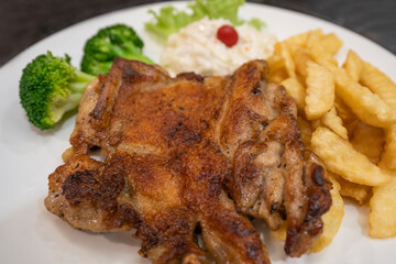 Grilled chicken chop with french fries ,salad, and broccoli on the plate.