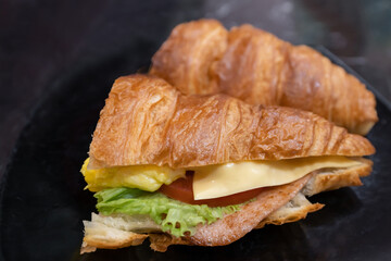 Close-up view of a croissant with chicken ham ,tomato slice, cheese slice and salad coral.