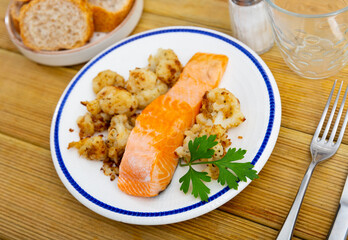 Hearty and dietary lunch is served, fried salmon fillet and cauliflower inflorescences in crispy crust. Dish cooked on electric grill at home, according to traditional Italian recipe.