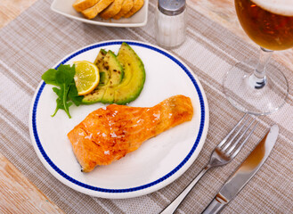 Salmon steak with avocado, lemon and herbs on a plate. Fish fillet with a golden crust for lunch.