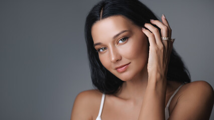 Fototapeta premium A beautiful young woman with radiant, flawless skin and natural makeup gently touches her hair. This high-quality image is ideal for beauty, skincare, and lifestyle product promotions or tutorials.