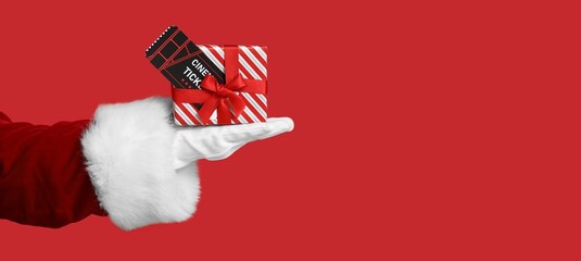 Santa's hand holding cinema ticket and gift box on red background with space for text