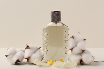 Bottle of perfume with petals and cotton flowers  on beige background