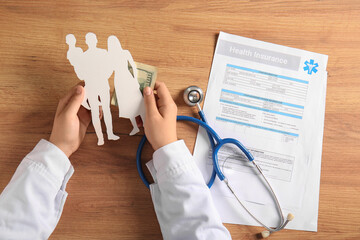 Female doctor hands holding family silhouette near health insurance form and stethoscope on wooden...