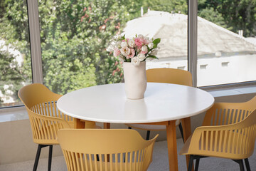Dining table with flowers near window in room