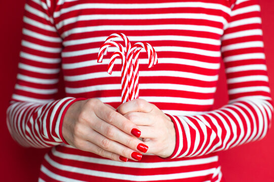 Hands of white woman with red manicure holding Christmas candy canes 
