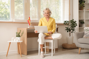 Mature woman in headphones with laptop learning Spanish online at home