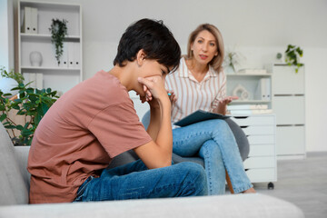 Obraz premium Upset teenage boy sitting on sofa at psychologist's office