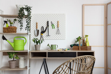 Workplace with gardening tools and plants near white wall