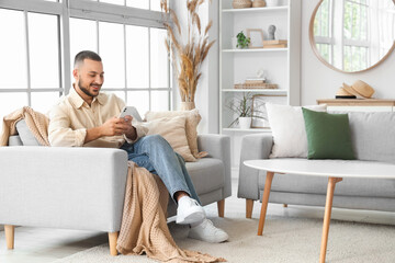 Young man chatting with mobile phone on comfortable sofa at home