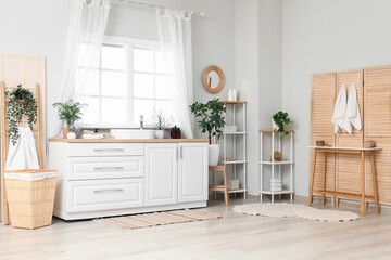 Interior of stylish bathroom with sink, chest of drawers and folding screen near window