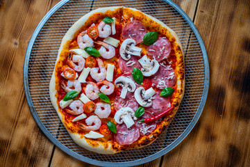Pizza from two halves: one with pepperoni and mushrooms, the other with shrimp and tomatoes. Pizza on a baking wheel on a wooden table. Space for text. High quality photo