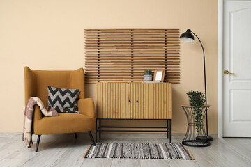 Soft armchair, wooden chest of drawers, lamp and folding screen in interior of beautiful living room