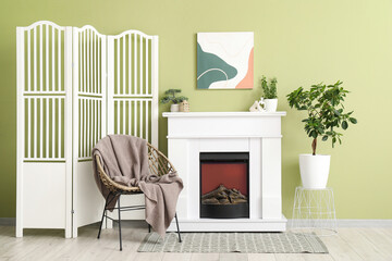 White fireplace, houseplants, armchair and folding screen in interior of stylish living room