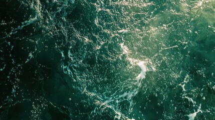 featuring a textured surface of dark green water, with soft waves and tiny splashes illuminated by sunlight. The water appears crystal clear,