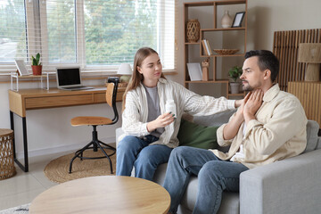 Young woman giving pill bottle to her husband with thyroid gland problem at home