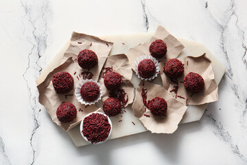 Board with delicious chocolate truffles and torn pieces of paper on light background