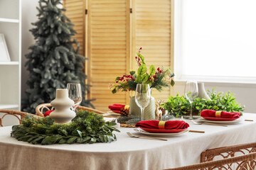 Beautiful festive table setting for Christmas celebration with wreaths in dining room