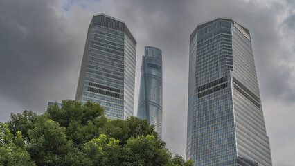 Naklejka premium Skyscrapers against a background of blue sky and clouds. Tall modern towers with glazed facades. Green vegetation. China.