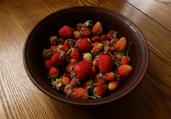 Delicious red fresh strawberries in a clay plate on a wooden table.
