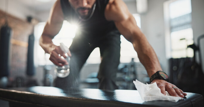 Man, hands and spraying with bottle on gym bench for hygiene, disinfection or sanitary equipment. Closeup, male person or cleaner wiping with sanitizer or detergent for bacteria or germ removal