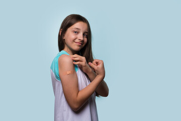 A young girl shows off her vaccinated arm by flexing and smiling, proudly wearing a bandage