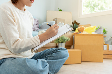 Move house, relocation. Woman using household checklist for new apartment Inside the room are...