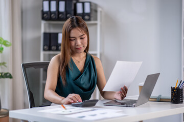 asian business woman working in office checking documents. young businesswoman accounting manager executive or lawyer using laptop reading paper file financial report, tax invoice.
