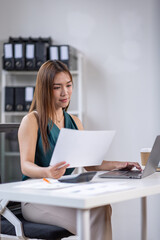 asian business woman working in office checking documents. young businesswoman accounting manager executive or lawyer using laptop reading paper file financial report, tax invoice.
