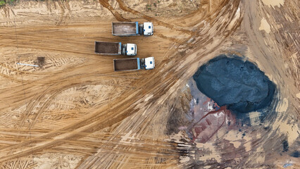Three trucks stand in a quarry preparing to load bulk construction materials.