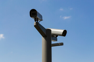 two security cameras mounted on a pole against a clear blue sky.
