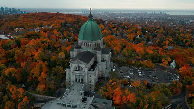 aerial shot around Saint Joseph Oratory in Montreal city revealing the city slyline in the backgound and the colorful landscape during fall season, Quebec Province, Canada