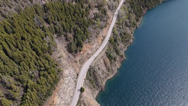 Car traveling on Ruote 40 winding along a tranquil glacial Lakar lake shore, embraced by national park vibrant green forest, Patagonia, Argentina, drone follow shot