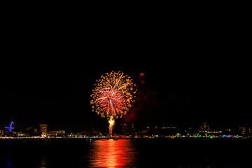 Brilliant red fireworks explode against a dark night sky, illuminating a cityscape below. Vibrant...