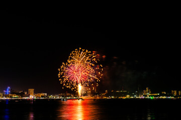Brilliant red fireworks explode against a dark night sky, illuminating a cityscape below. Vibrant...
