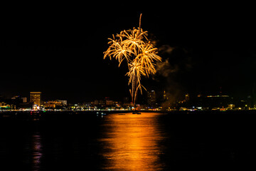 Naklejka premium Brilliant red fireworks explode against a dark night sky, illuminating a cityscape below. Vibrant bursts and smoke create a festive, dynamic atmosphere, capturing the excitement of celebration.