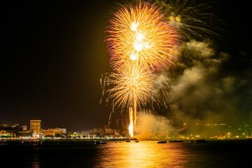Brilliant red fireworks explode against a dark night sky, illuminating a cityscape below. Vibrant...