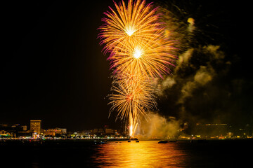 Brilliant red fireworks explode against a dark night sky, illuminating a cityscape below. Vibrant...