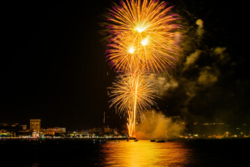 Brilliant red fireworks explode against a dark night sky, illuminating a cityscape below. Vibrant...