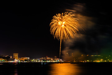 Brilliant red fireworks explode against a dark night sky, illuminating a cityscape below. Vibrant...