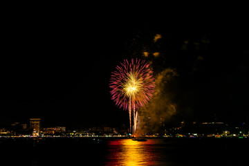 Brilliant red fireworks explode against a dark night sky, illuminating a cityscape below. Vibrant...