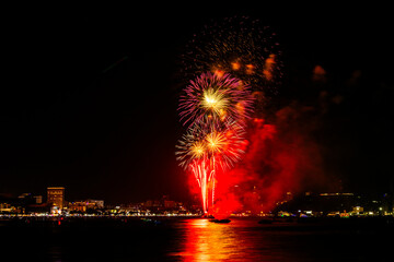 Brilliant red fireworks explode against a dark night sky, illuminating a cityscape below. Vibrant...