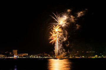 Brilliant red fireworks explode against a dark night sky, illuminating a cityscape below. Vibrant...