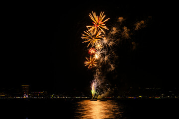 Brilliant red fireworks explode against a dark night sky, illuminating a cityscape below. Vibrant...